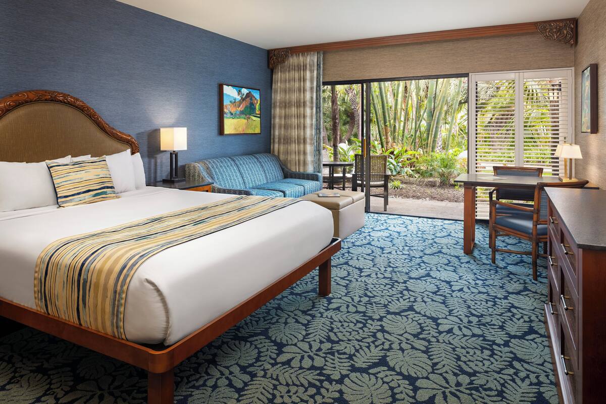 A hotel room with a large bed, a sofa, a desk, and a view of the outdoors.