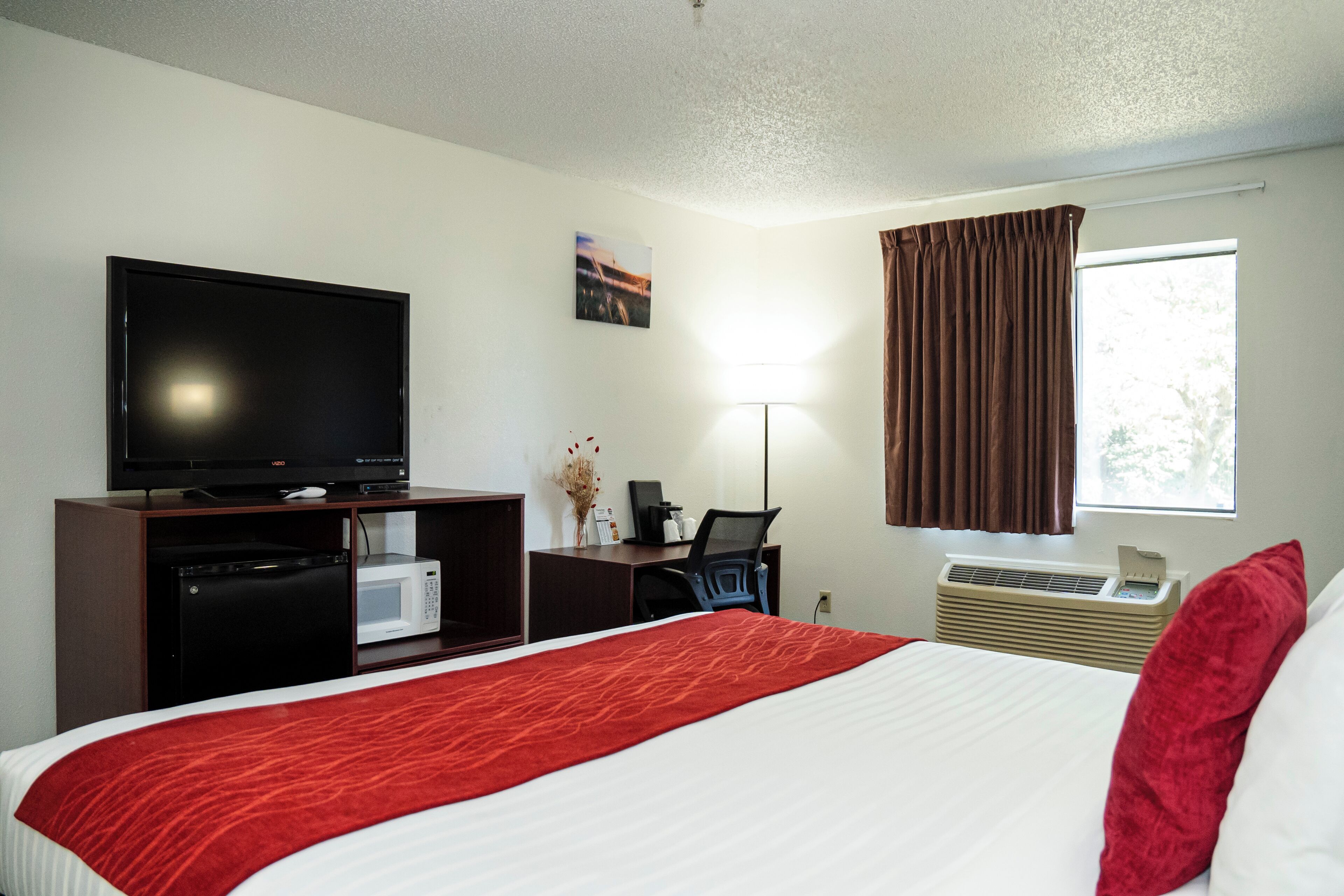 Habitación de hotel con cama, televisión, escritorio con computadora, microondas y aire acondicionado.