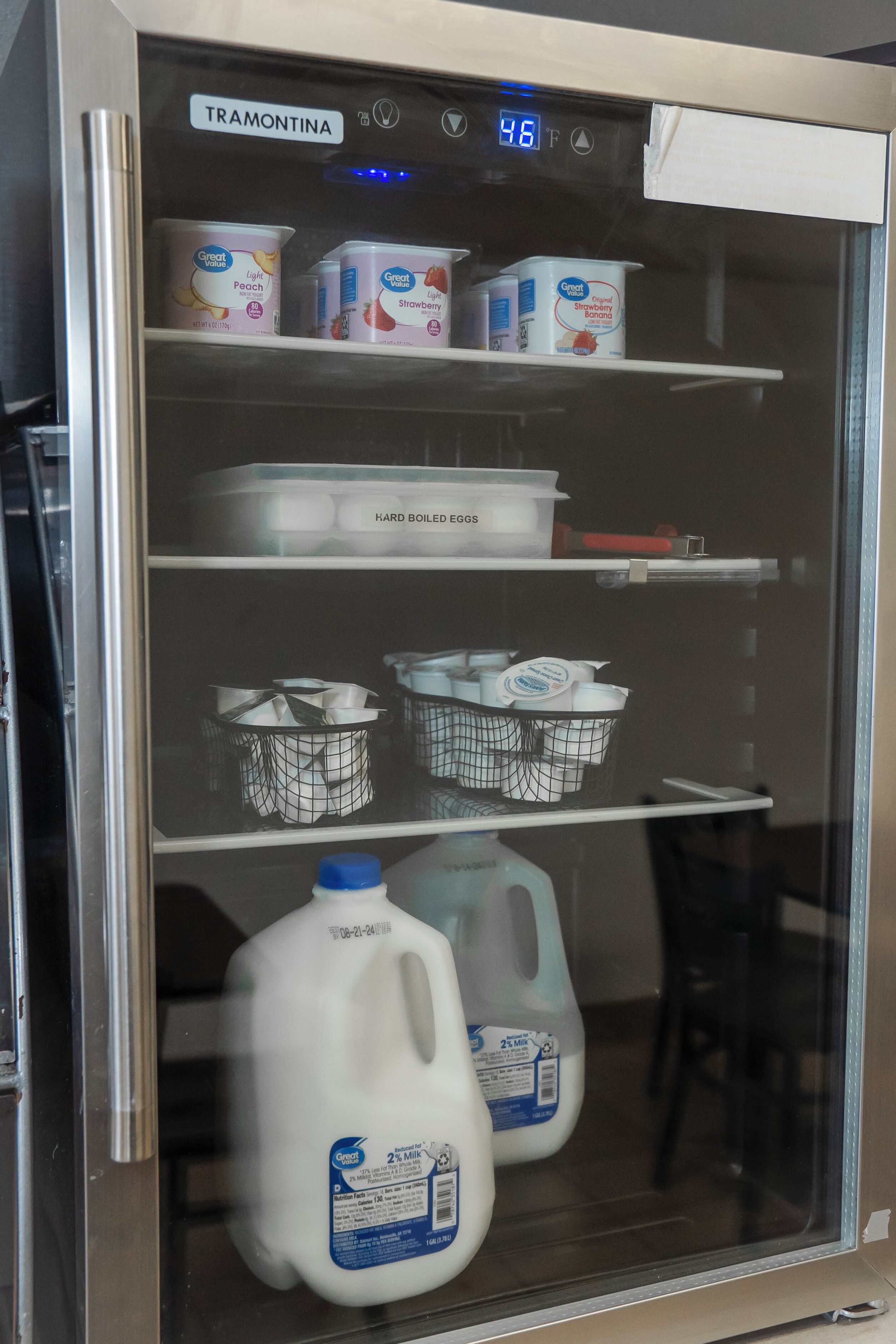 A refrigerator with shelves containing Great Value light peach and strawberry yogurt, hard-boiled eggs, and milk jugs.