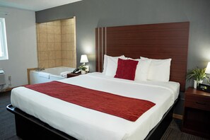 A hotel room with a large bed, a wooden headboard, a bedside table with a lamp, and a small potted plant.