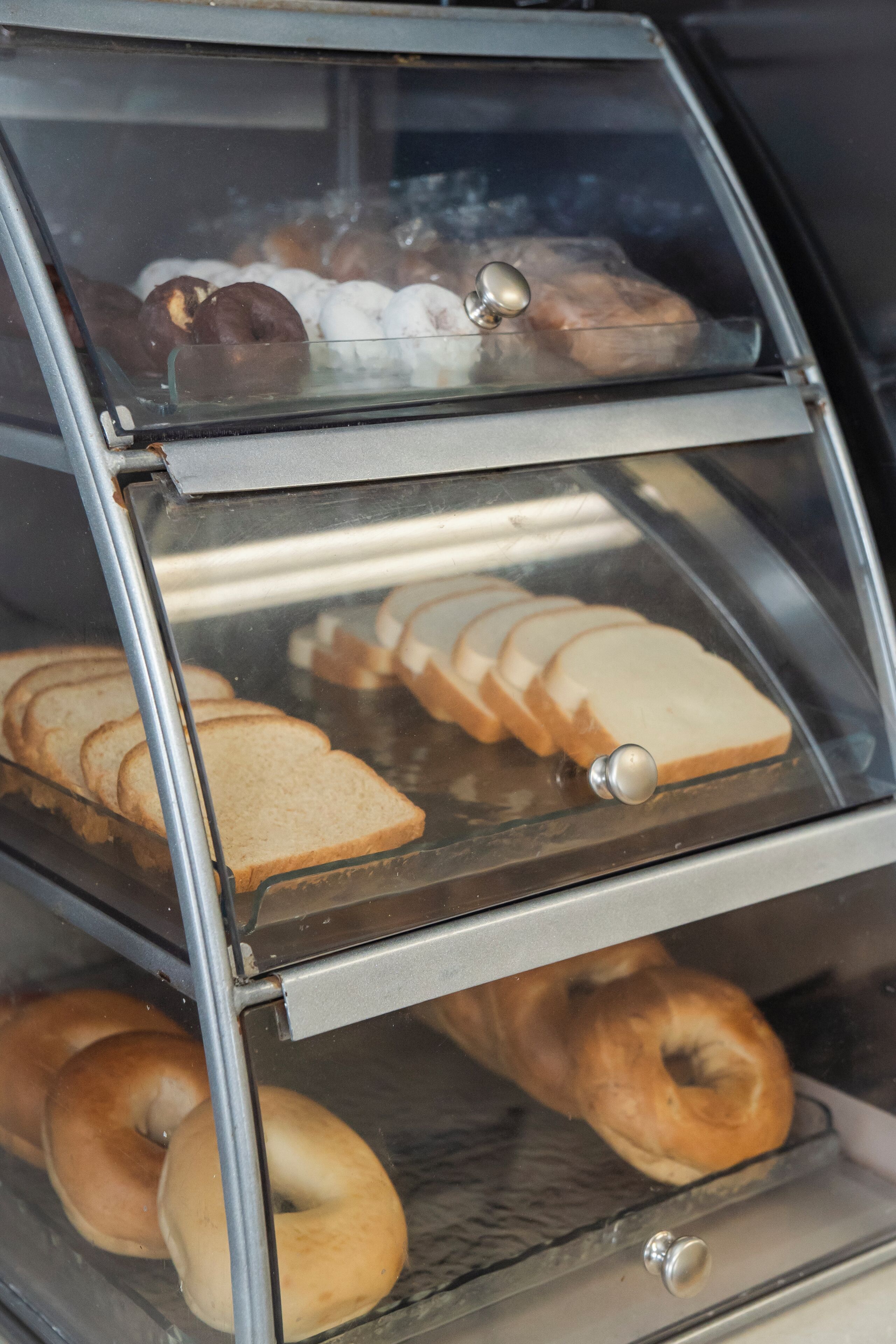 Vitrina de panadería con diversos productos horneados, incluyendo bagels y pan en rodajas.