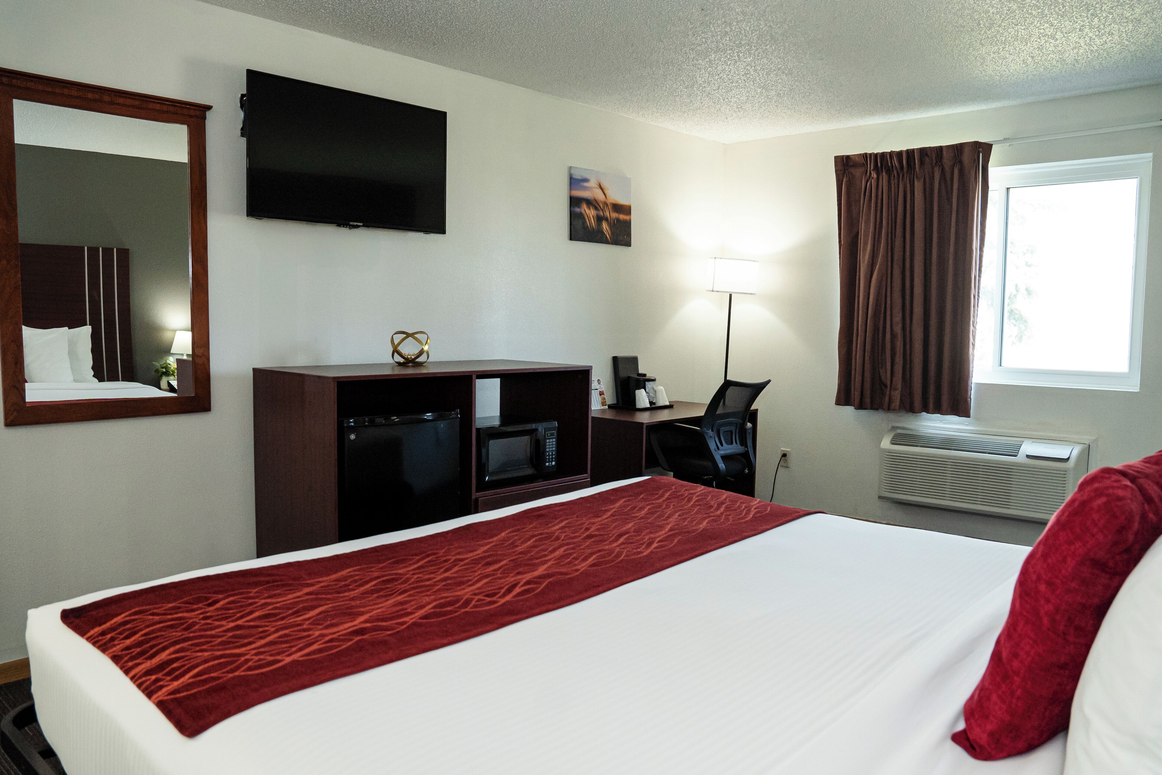 A hotel room with a large bed, a desk with a computer, a flat-screen TV, a microwave, and an air conditioner.