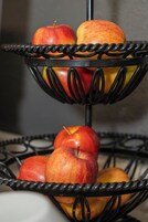 Un frutero metálico de tres niveles con manzanas.