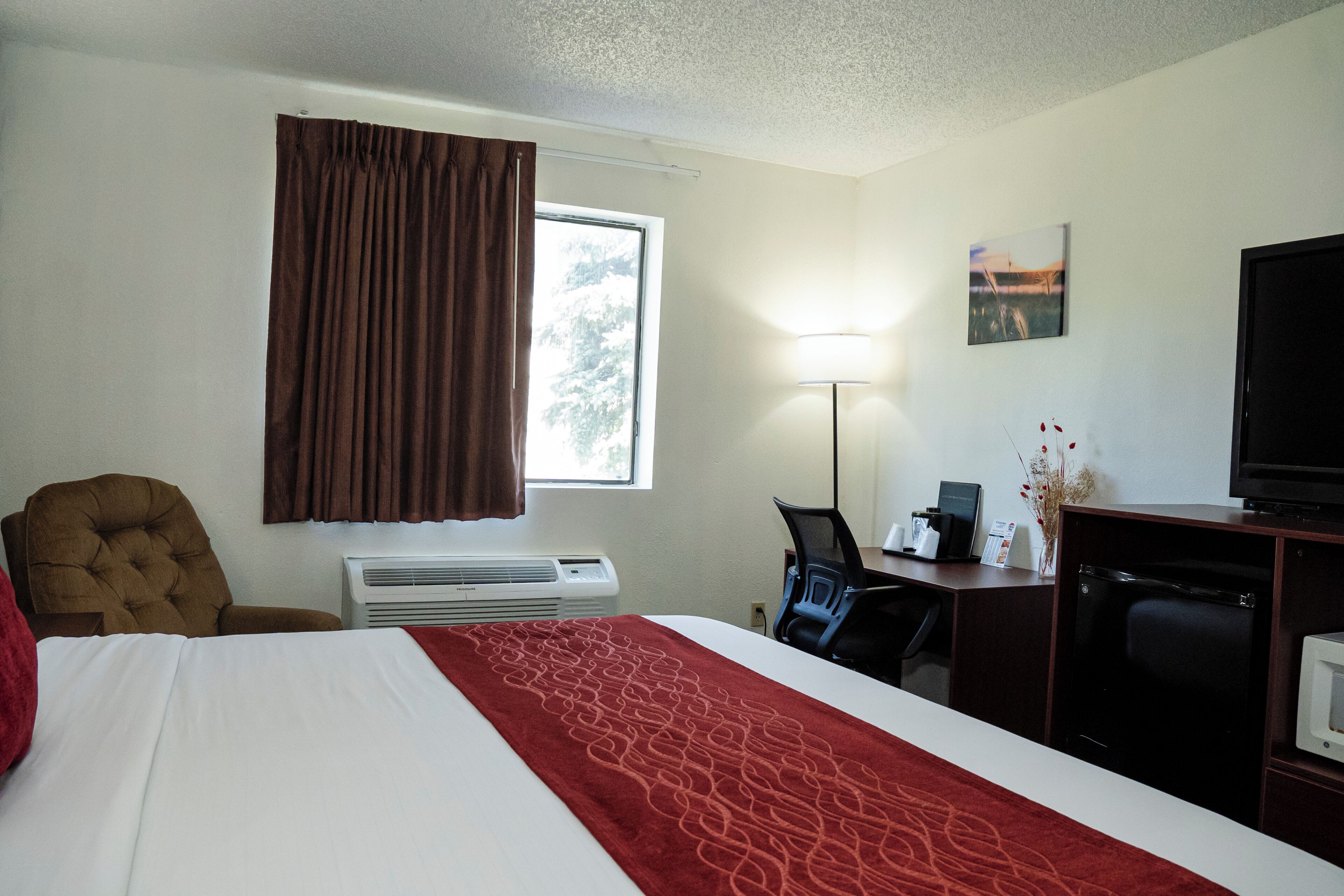 Habitación de hotel con cama, escritorio, silla, televisión y ventana con cortinas.