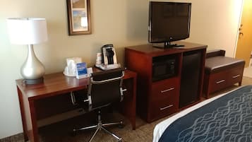 Une chambre d’hôtel avec un bureau en bois, une chaise, une télévision, une machine à café, un four à micro-ondes, un petit placard et un lit recouvert d’une couverture à motifs.