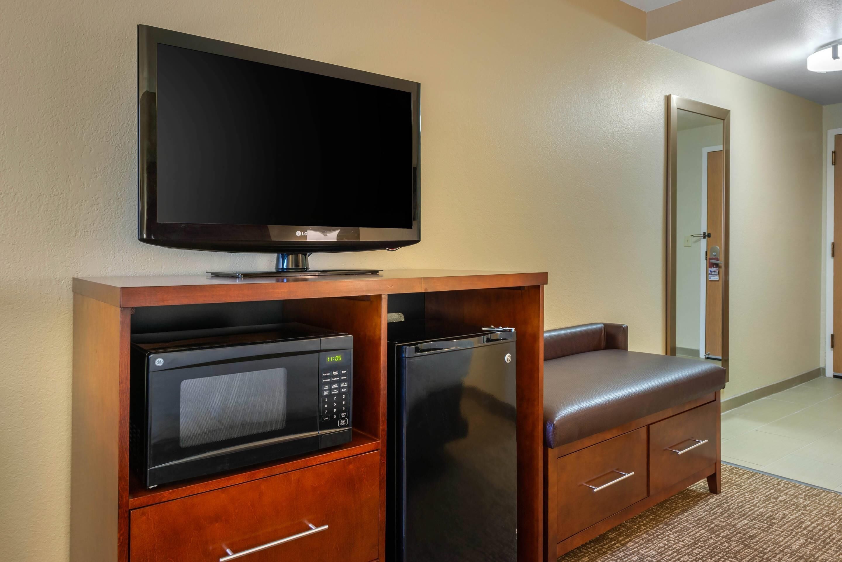 A compact kitchenette with a microwave, refrigerator, and a flat-screen TV on a wooden cabinet.