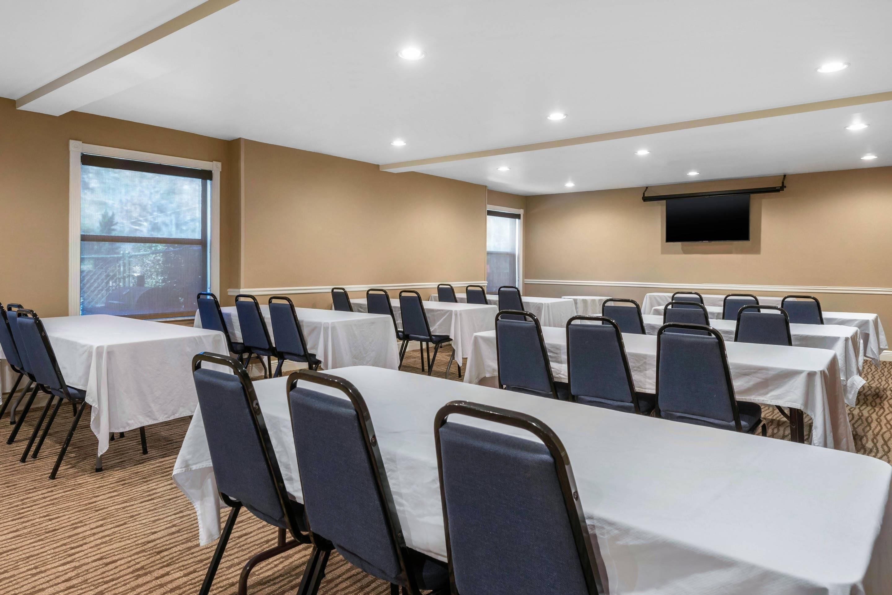 A conference room with multiple tables and chairs, a large window, and a flat-screen TV mounted on the wall.