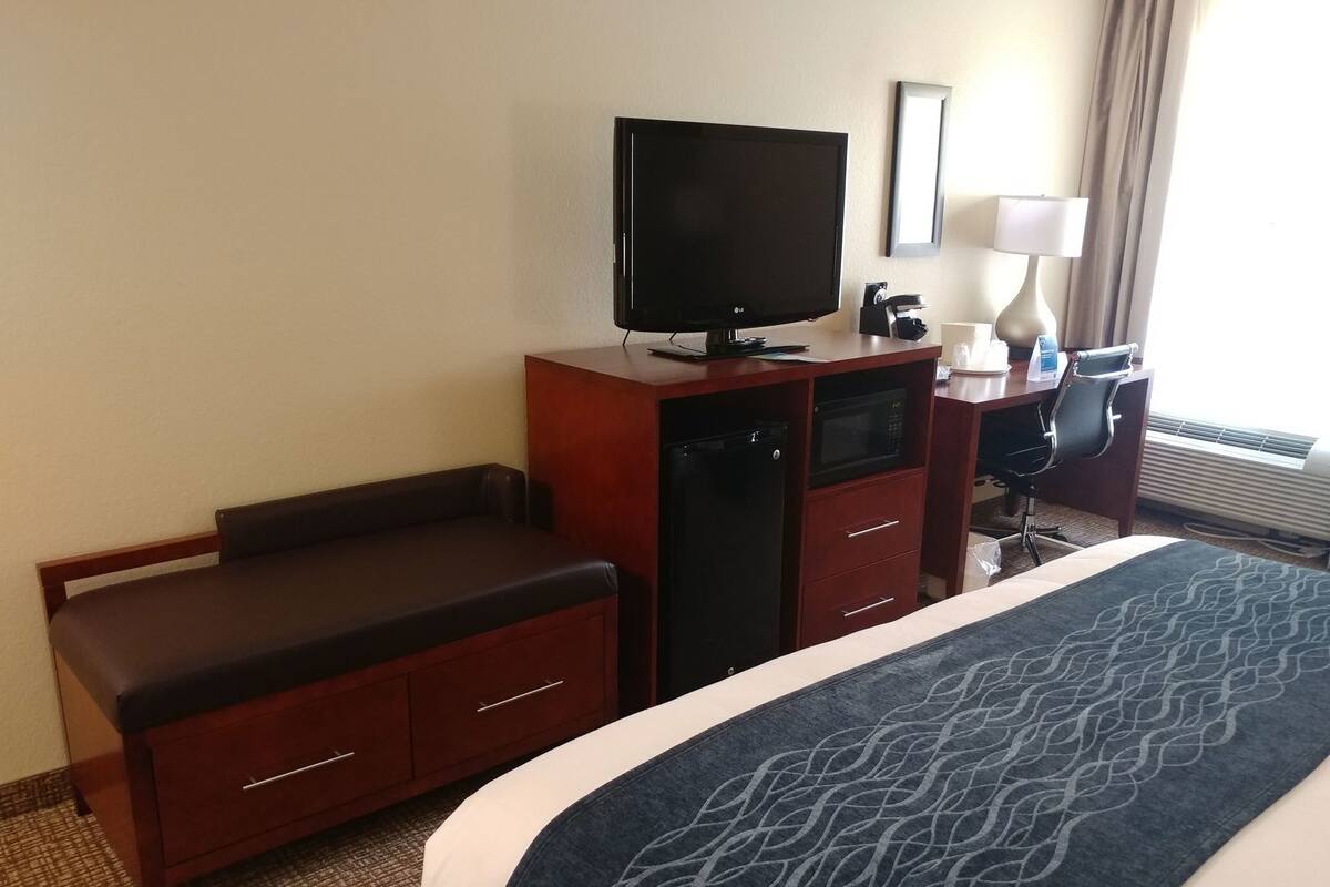 A hotel room with a bed, a desk with a flat-screen TV, a microwave, and a coffee maker.