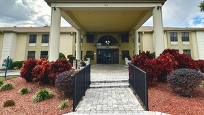 A building with a covered entrance, numbered 1212, surrounded by landscaped gardens with red and purple shrubs. - Comfort Inn Ocala Silver Springs (Ocala)