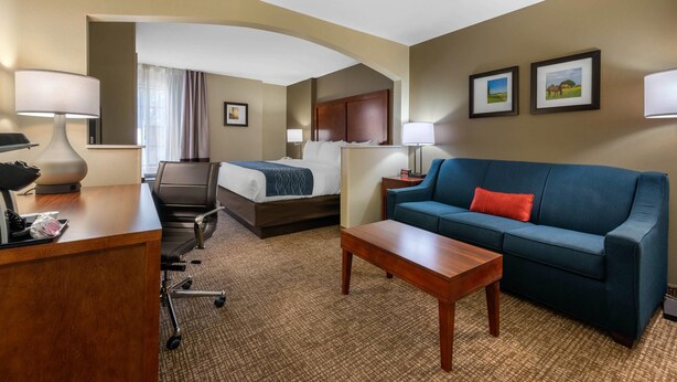 A hotel room with a bed, a blue sofa, a wooden desk, and a small table. - Comfort Inn Ocala Silver Springs (Ocala)