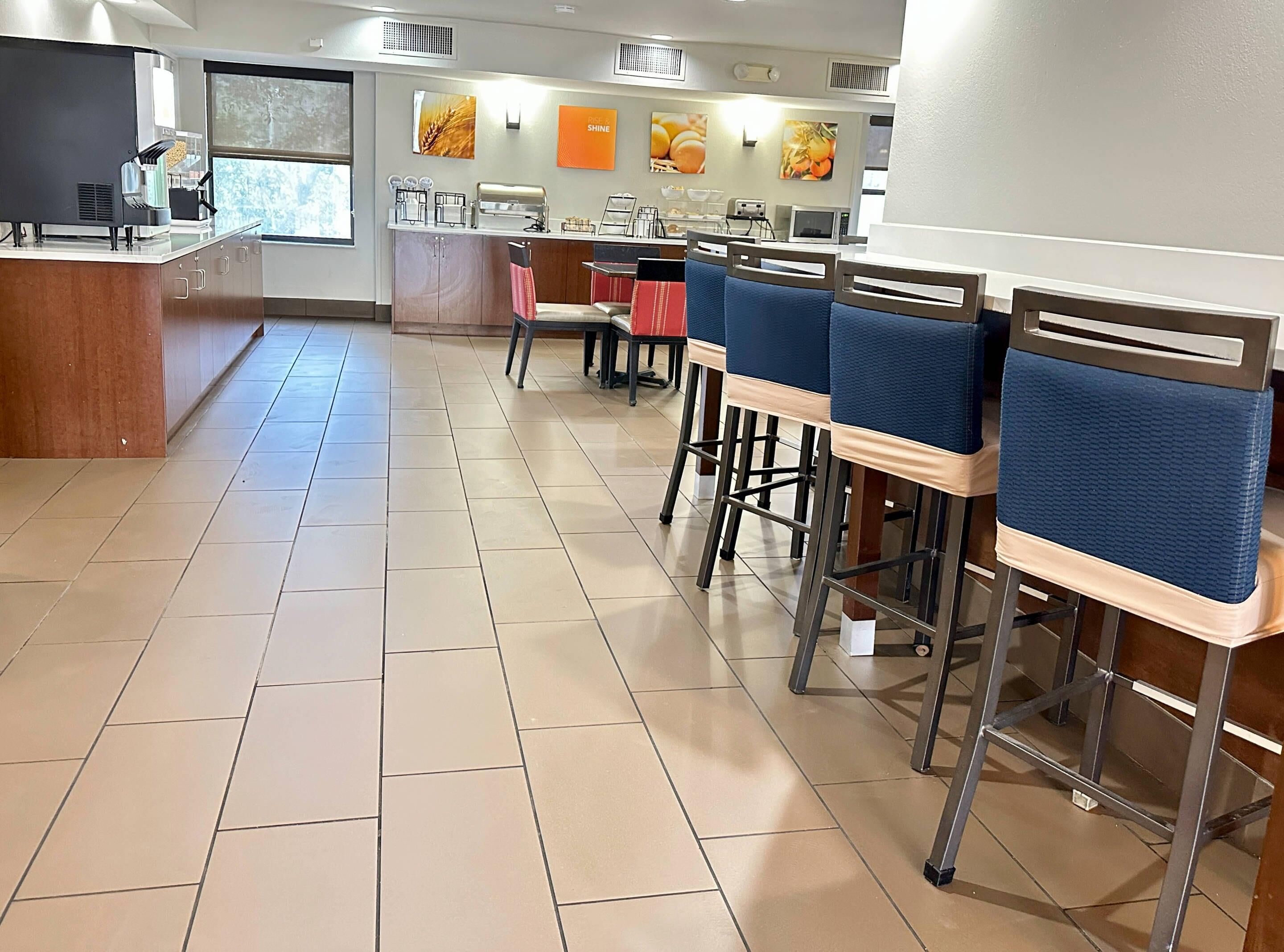 A clean, modern cafe with a long counter, blue cushioned chairs, and a tiled floor.