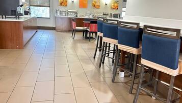 A clean, modern cafe with a long counter, blue cushioned chairs, and a tiled floor.