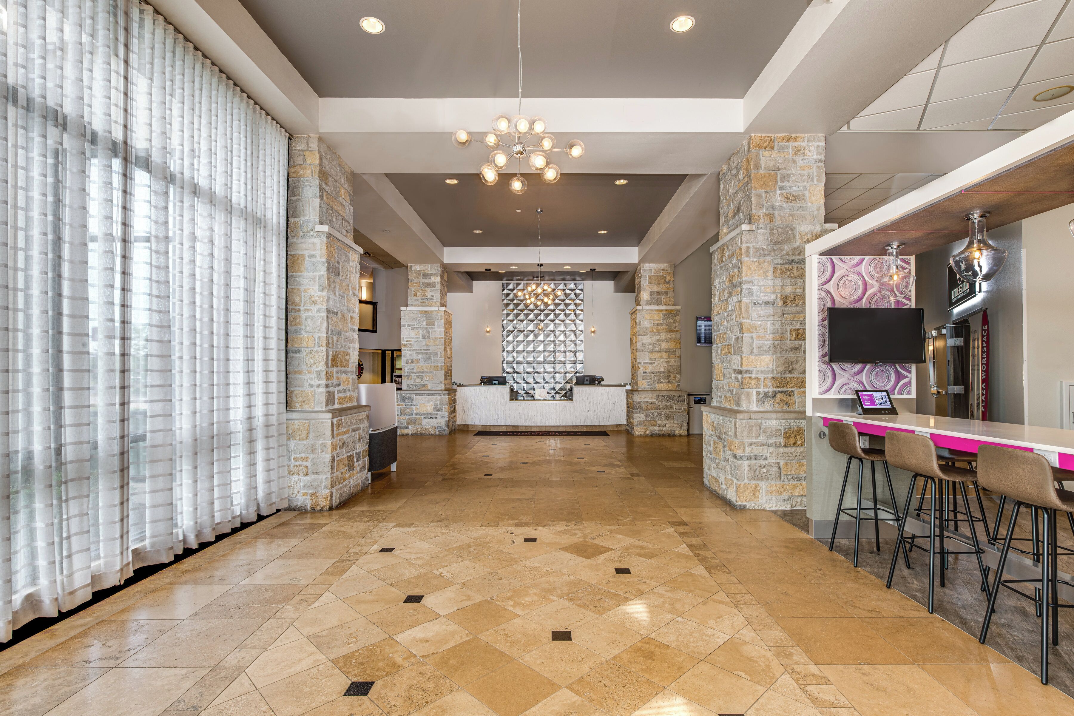 A hotel lobby with a reception desk, stone pillars, a chandelier, and a bar area.