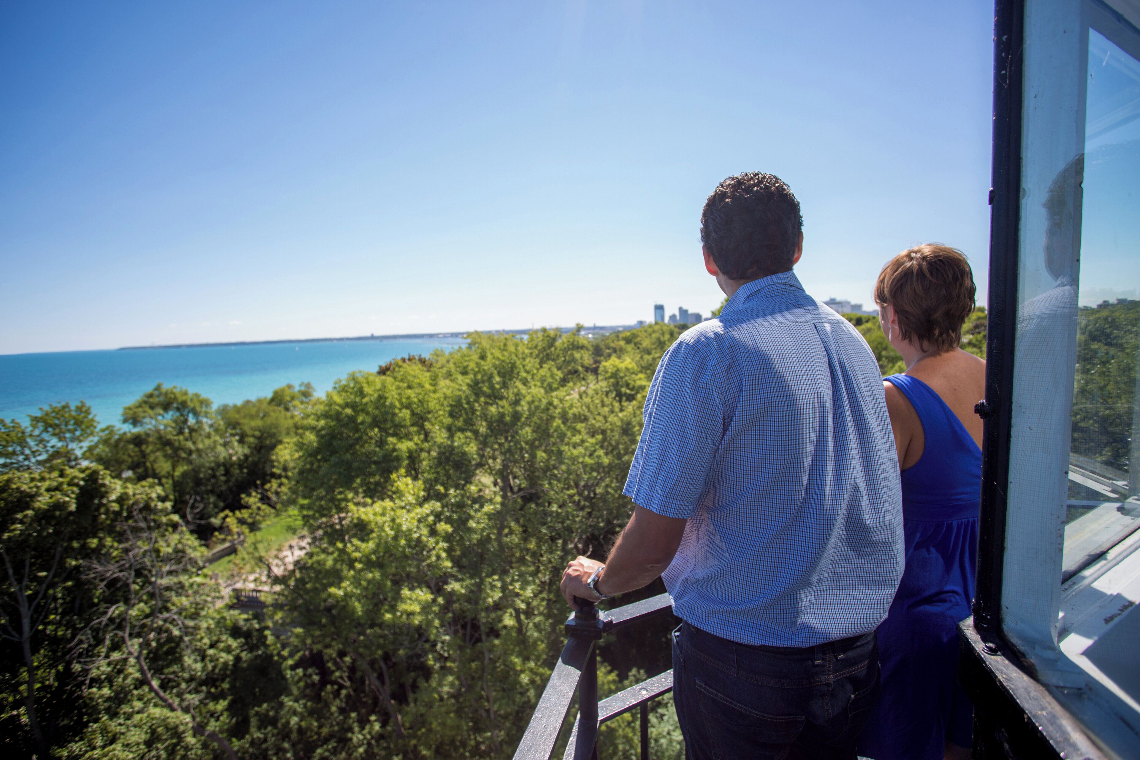 A man and a woman looking out from a window with a view of a body of water and greenery.
