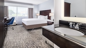 Habitación de hotel con cama, escritorio, silla, espejo grande y baño con lavamanos y espejo.