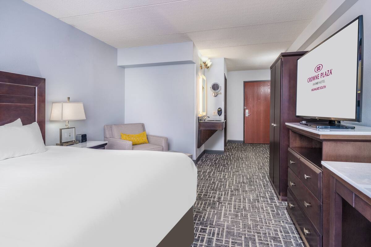 Une chambre d’hôtel avec un grand lit, un bureau avec un ordinateur, une chaise, un miroir et un téléviseur.