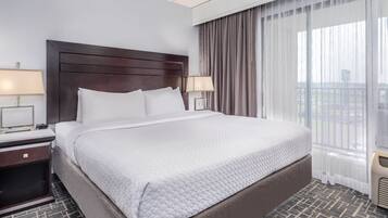 A hotel room with a large bed, two bedside tables with lamps, a window with sheer curtains, and a view of the outside.