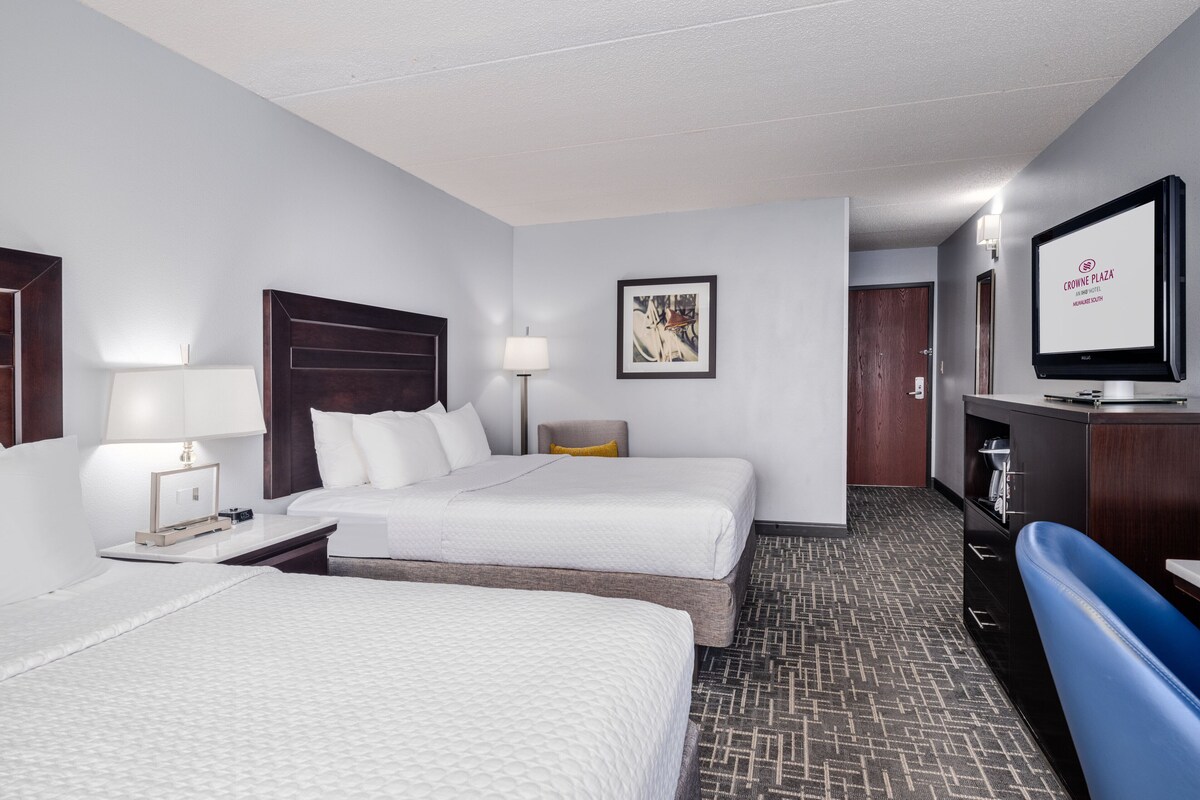 A hotel room with two beds, a desk, a TV, and a sofa.