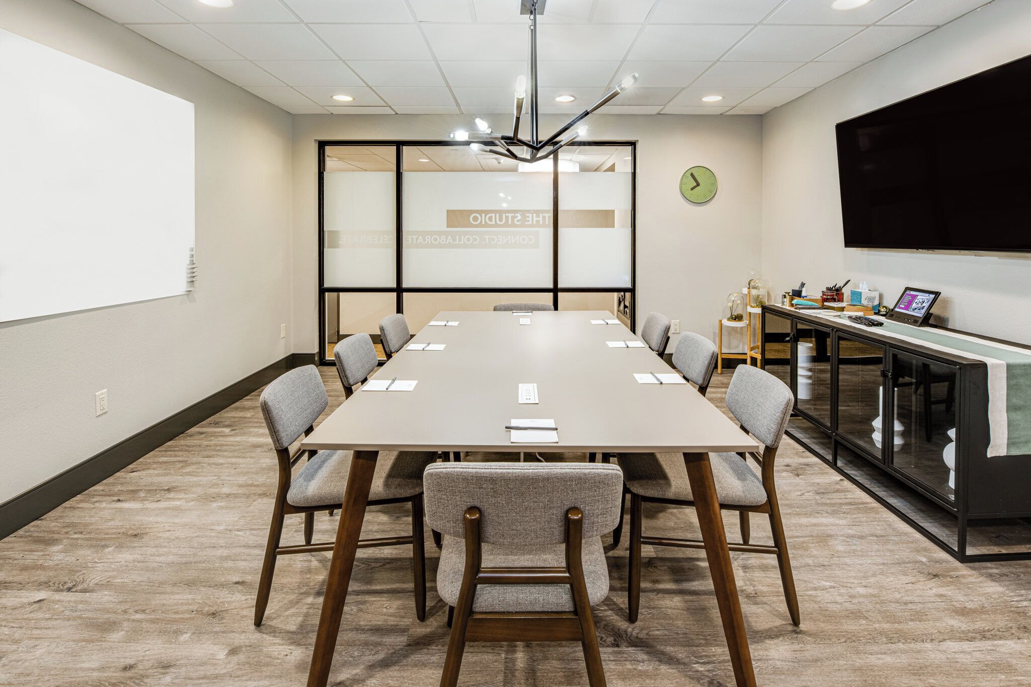 A conference room with a long table, chairs, a projector screen, and a clock on the wall.