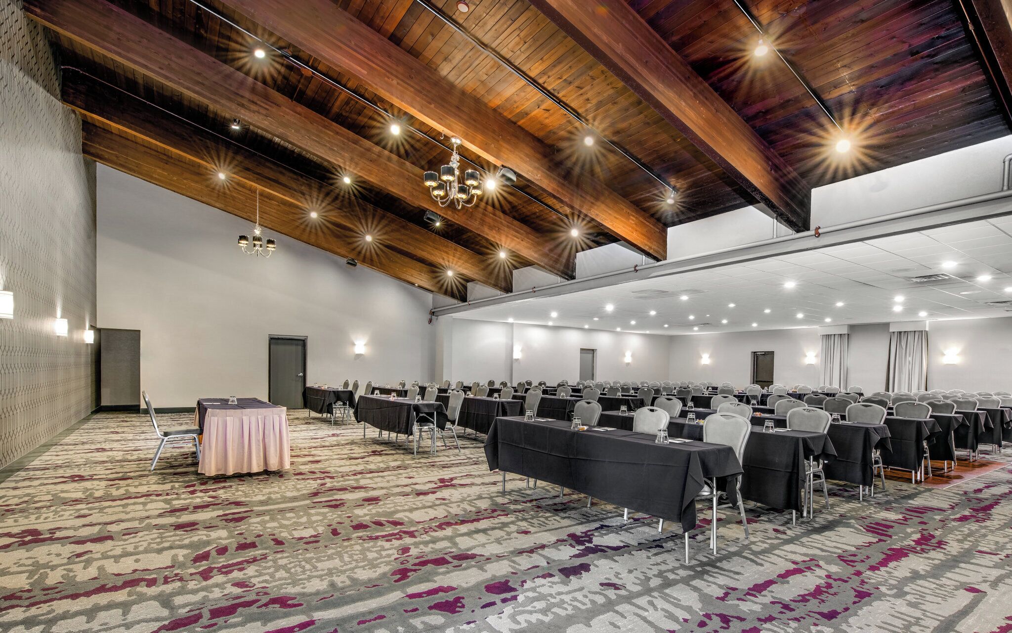 A conference room with rows of tables and chairs, a patterned carpet, and a wooden ceiling with exposed beams.