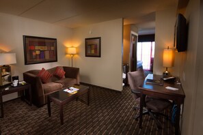 A hotel room with a brown sofa, a small table, a desk with a chair, and a TV mounted on the wall. - Crowne Plaza Milwaukee Airport by IHG (Milwaukee)