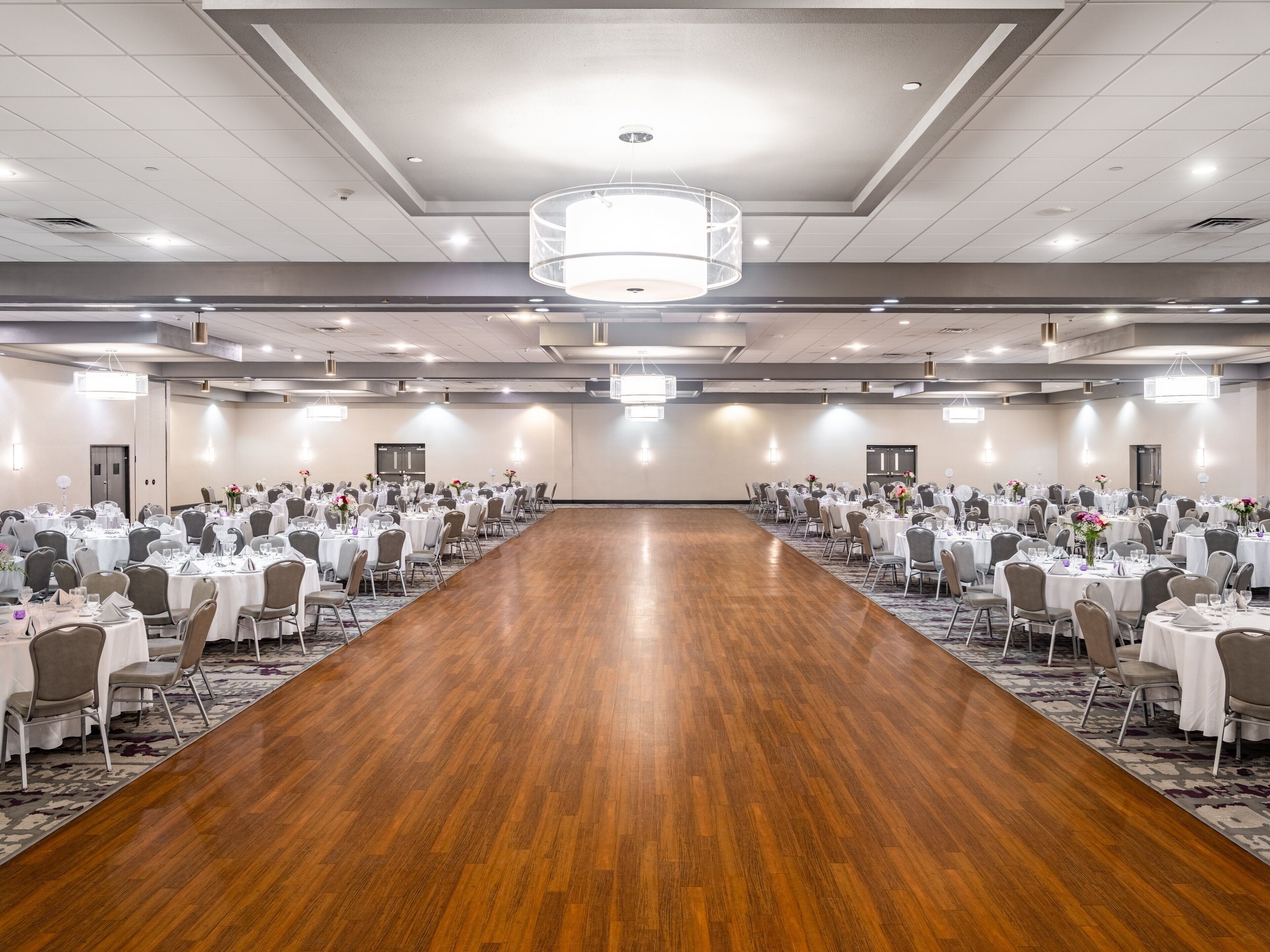 A large conference room with rows of tables and chairs, a wooden floor, and a chandelier.