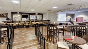 Zona de bar con varias opciones de asientos, incluyendo taburetes y mesas, y una escalera que lleva a un nivel superior.