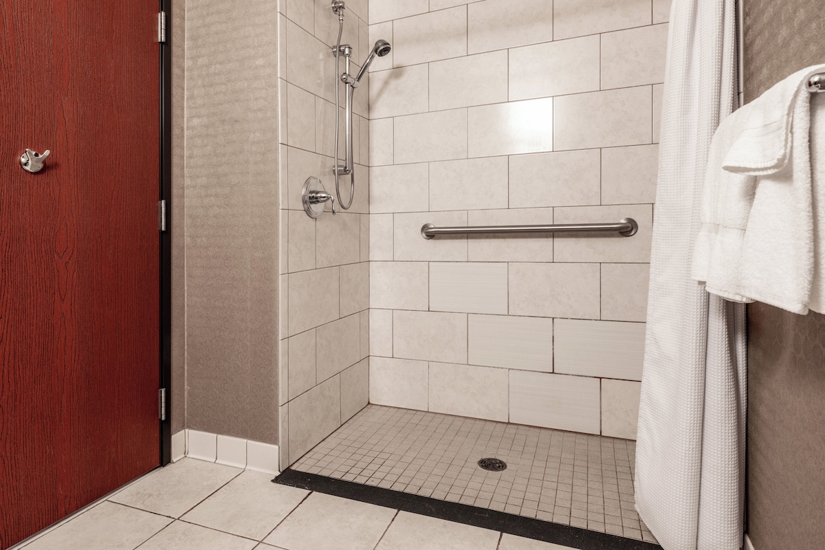 A shower area with a tiled floor, a handrail, and a towel hanging on the wall.