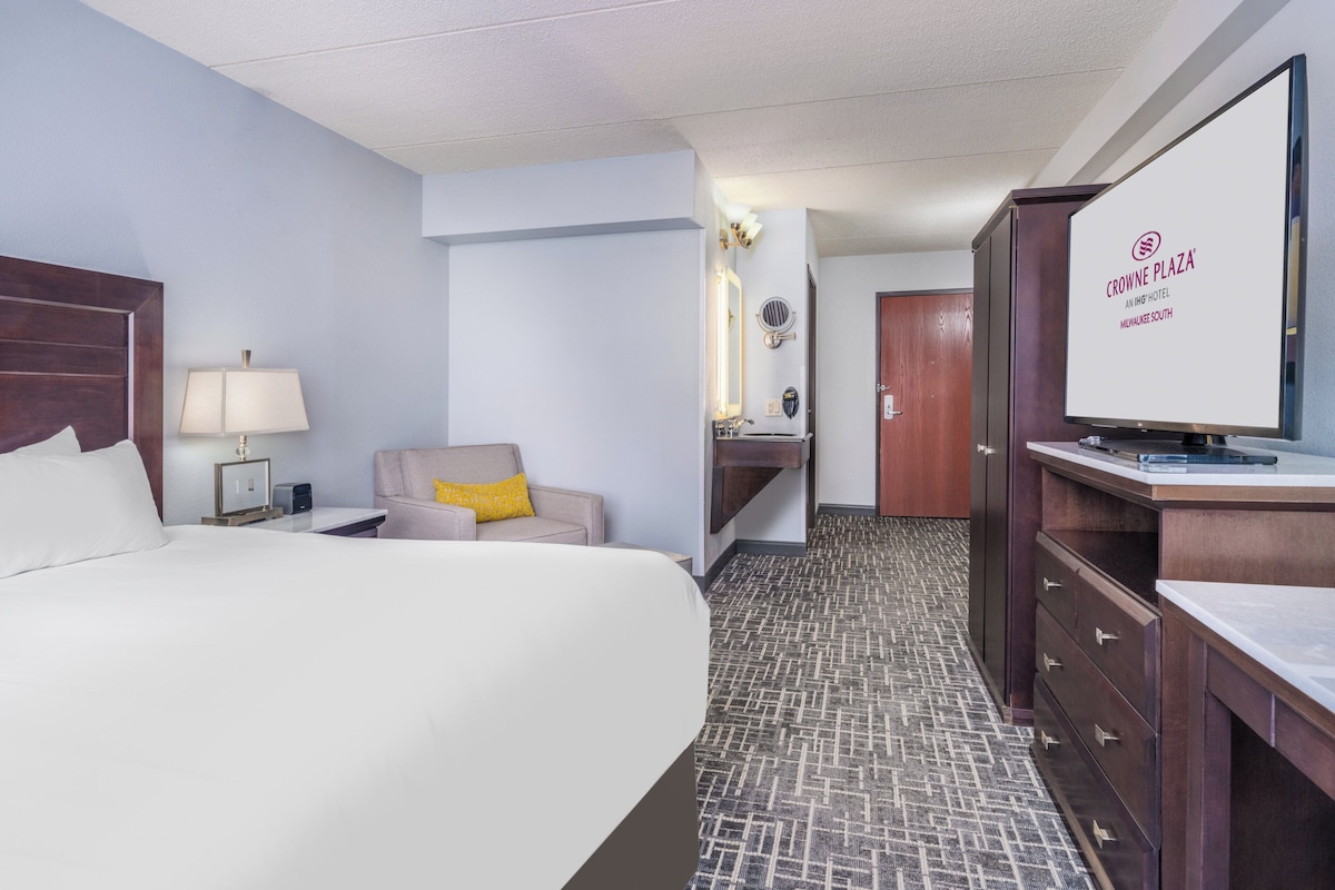 A hotel room with a large bed, a desk with a computer, a chair, a mirror, and a television.