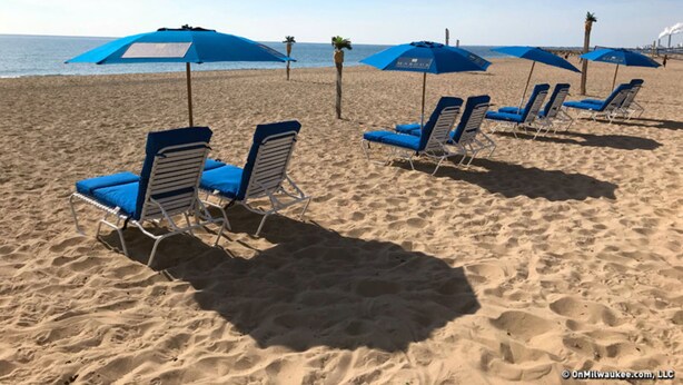 Una playa con hileras de sillas azules y sombrillas.