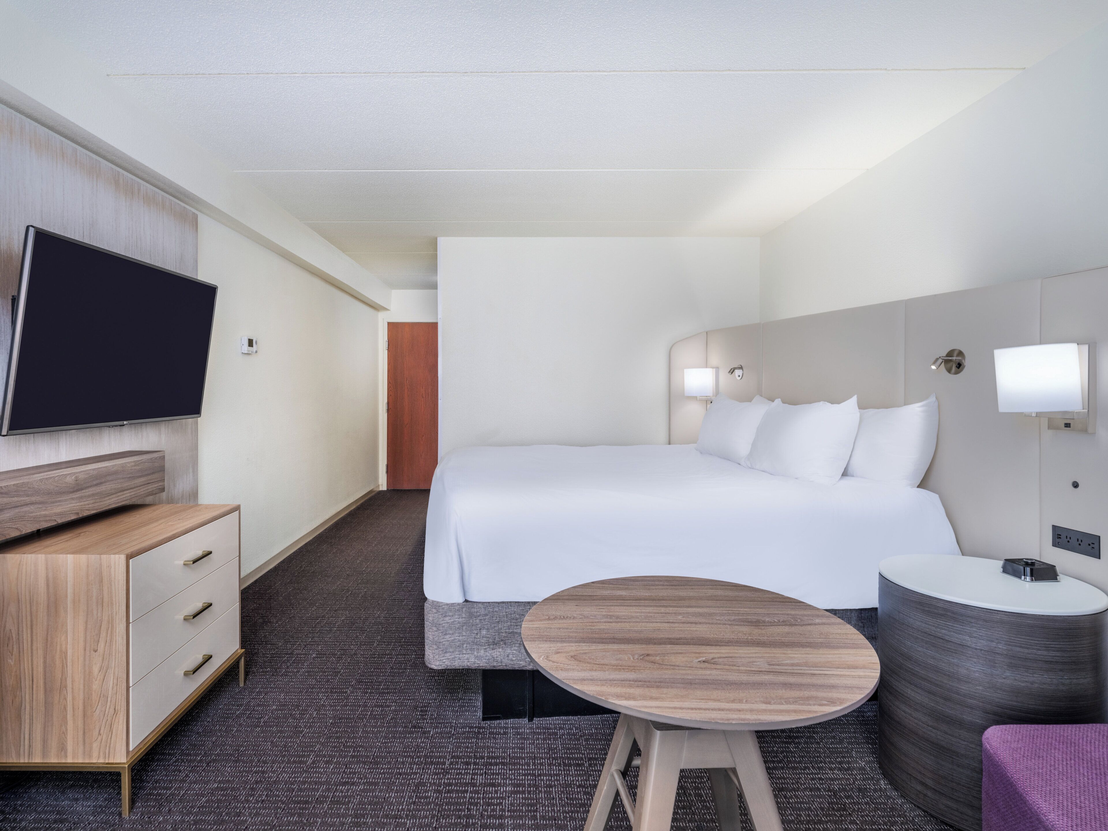 A hotel room with a bed, a TV, a desk, and a small table.