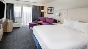 Habitación de hotel con una cama grande, un sofá, un televisor, un escritorio y una ventana con cortinas.