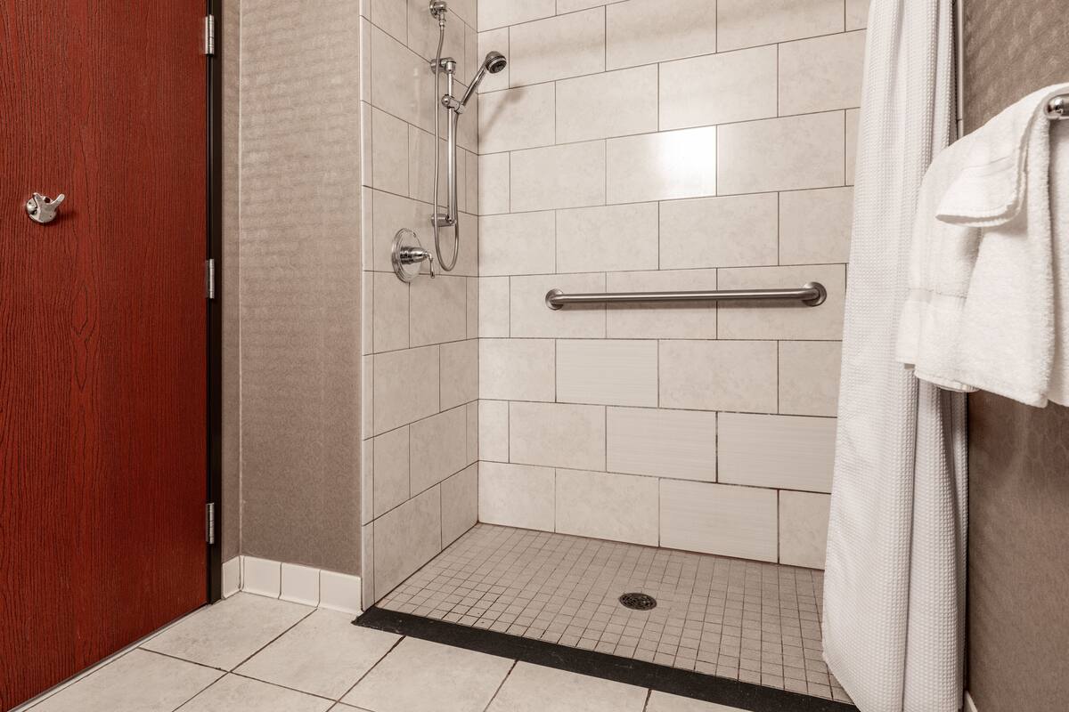 Un espace douche doté d’un sol carrelé, d’une barre d’appui et d’une serviette accrochée au mur.