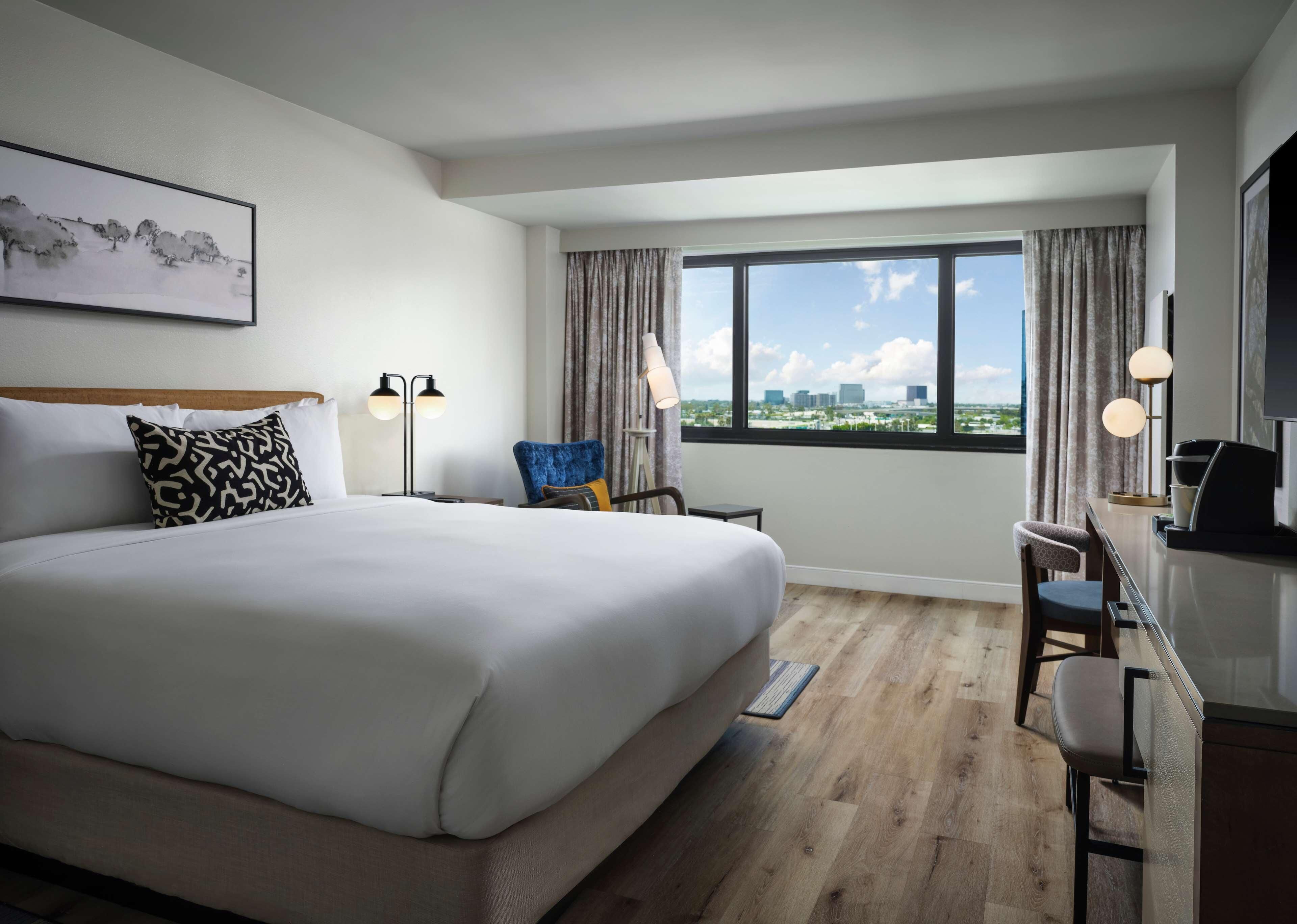 Une chambre d’hôtel avec un grand lit, un bureau, une chaise, une télévision et une fenêtre donnant sur la ville.