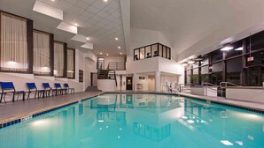 Une piscine intérieure à l’eau d’un bleu cristallin, un espace détente avec des chaises bleues et un escalier menant à un deuxième niveau.