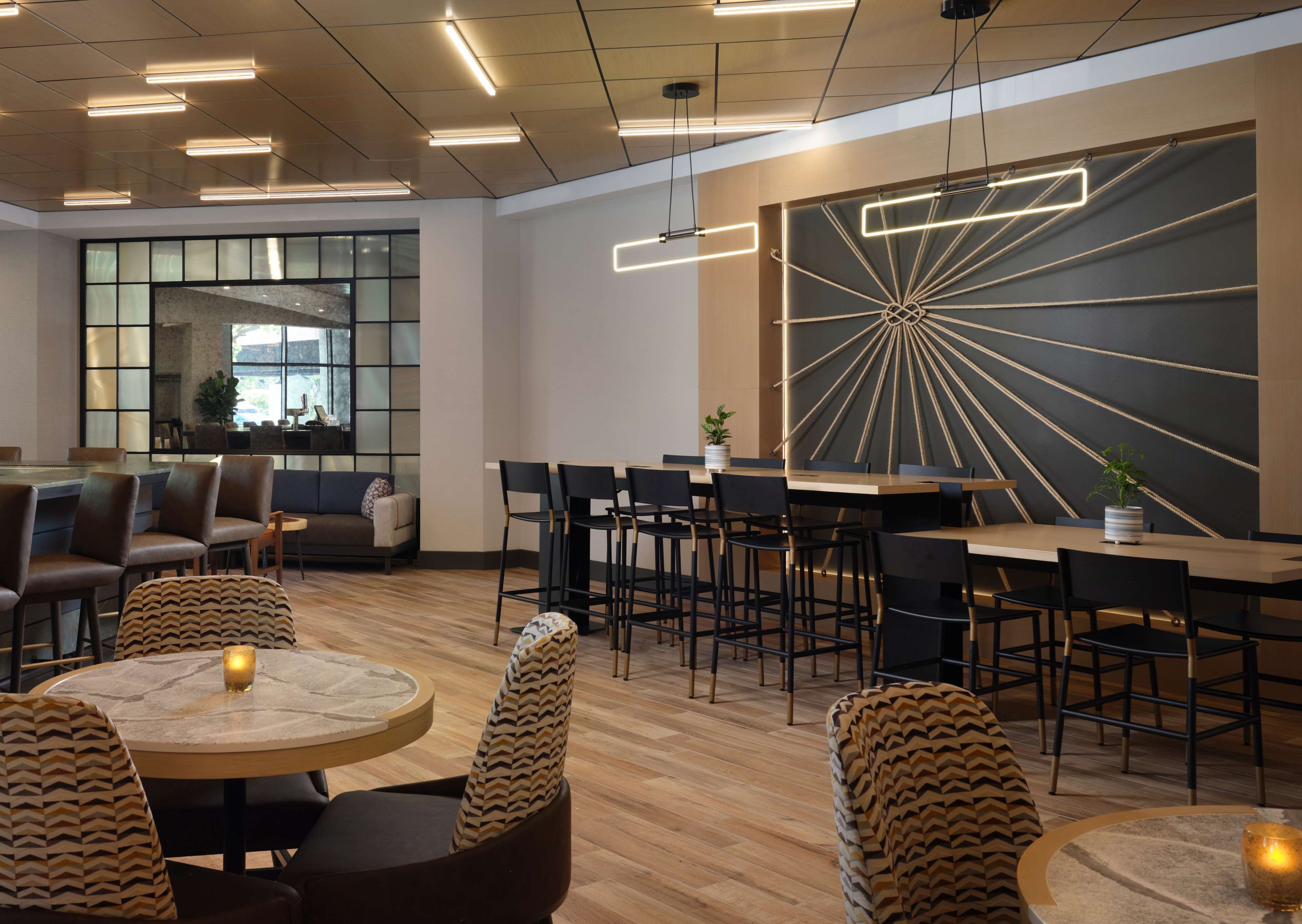 Un espace lounge moderne avec des tables rondes, des sièges de bar et une grande œuvre d’art murale.