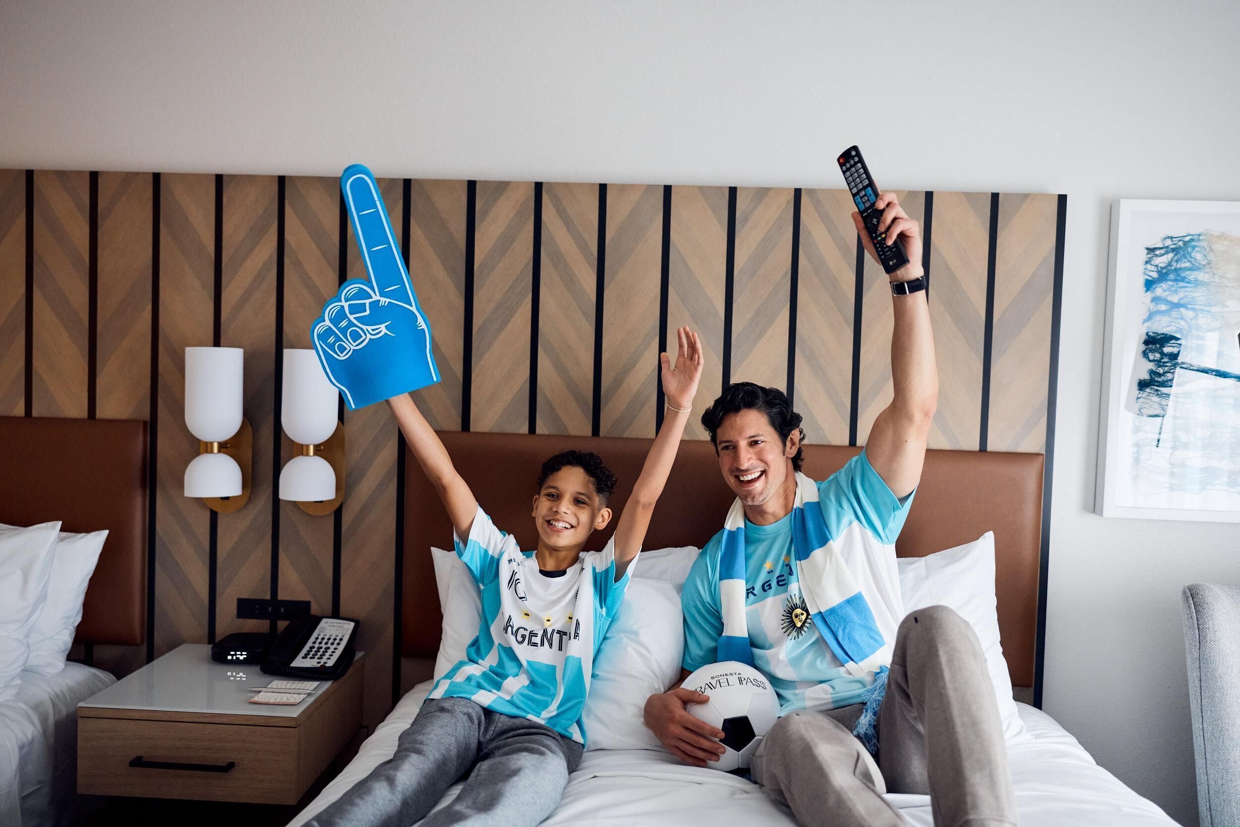 Una habitación de hotel con una cama, una mesita de noche con un teléfono y una lámpara de pared.