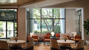 Un espacio interior amplio con diversas disposiciones de asientos, ventanas grandes que proporcionan luz natural y vistas a la vegetación exterior.