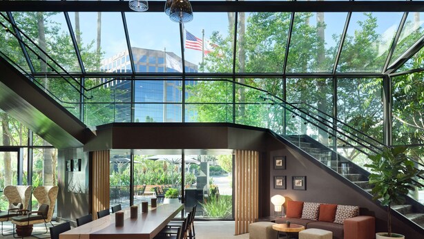 Un intérieur moderne avec un grand mur de verre, un coin repas avec une longue table et des chaises, un ensemble de canapés et un escalier.