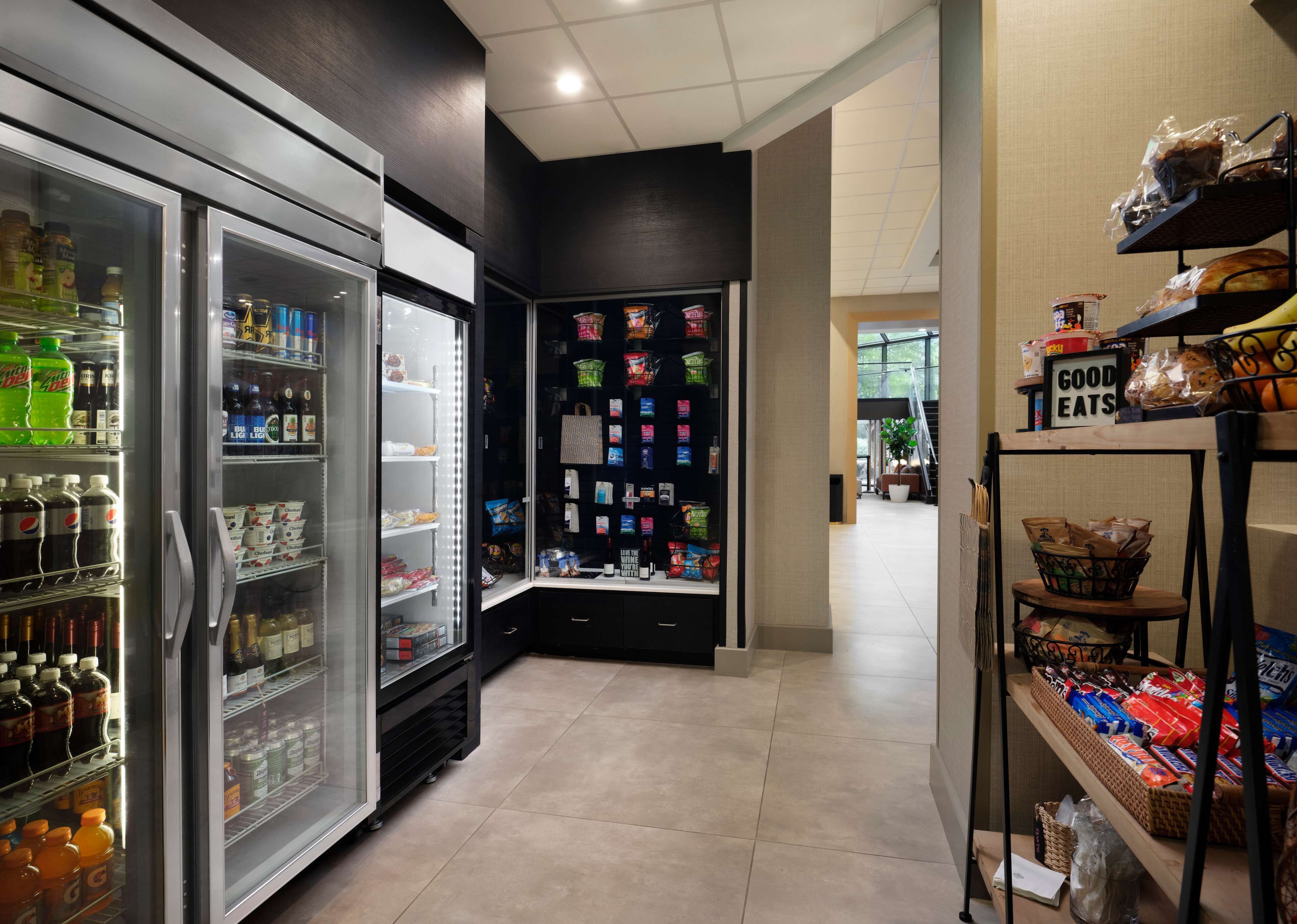 A corridor with a refrigerated beverage display, snack shelves, and a 'Good Eats' sign.