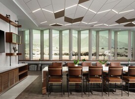 A modern dining area with a long table, multiple chairs, and a large window with a mountain view.