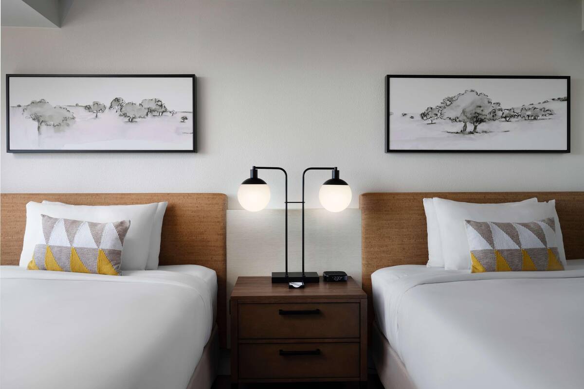 Une chambre d’hôtel avec deux lits, une table de chevet, une lampe et deux tableaux encadrés au mur.