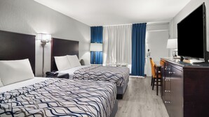 A hotel room with two beds, a desk with a TV, a chair, and a window with curtains.
