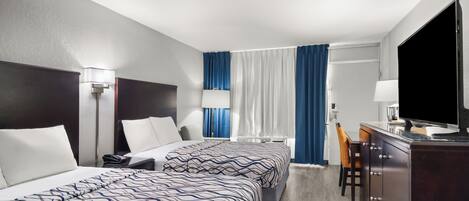 A hotel room with two beds, a desk with a TV, a chair, and a window with curtains.