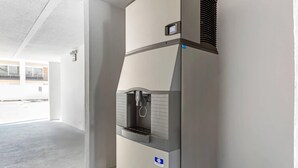 A water dispenser in a hallway with a concrete floor and a white wall.