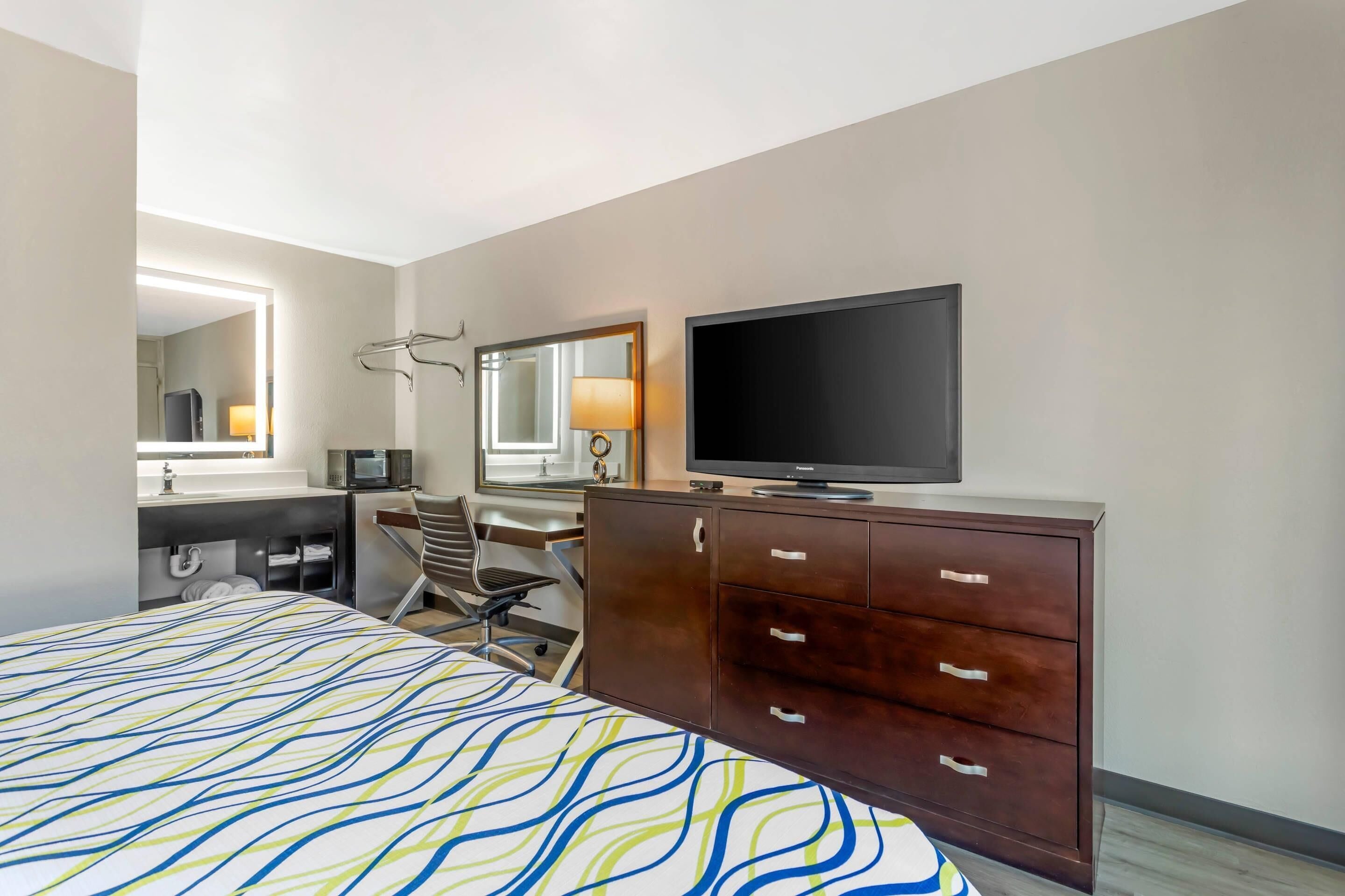 Een hotelkamer met een bed, een televisie, een bureau met stoel, een spiegel en een kast.