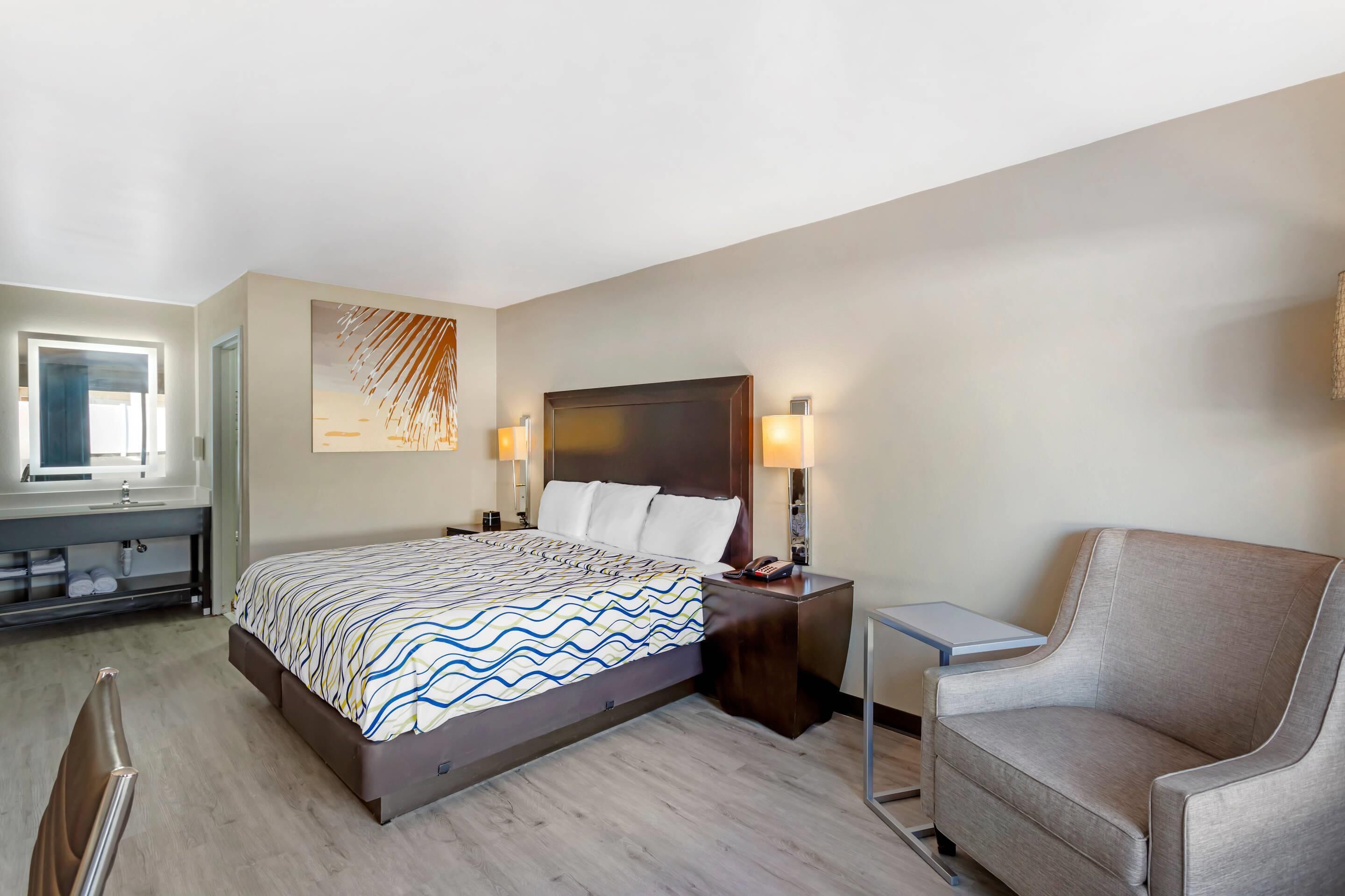 Una habitación de hotel con cama, mesita de noche, silla y una pequeña mesa con lámpara.