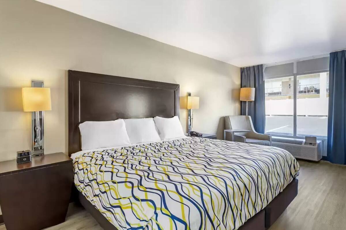 A hotel room with a large bed, two bedside tables, a chair, and a large window.