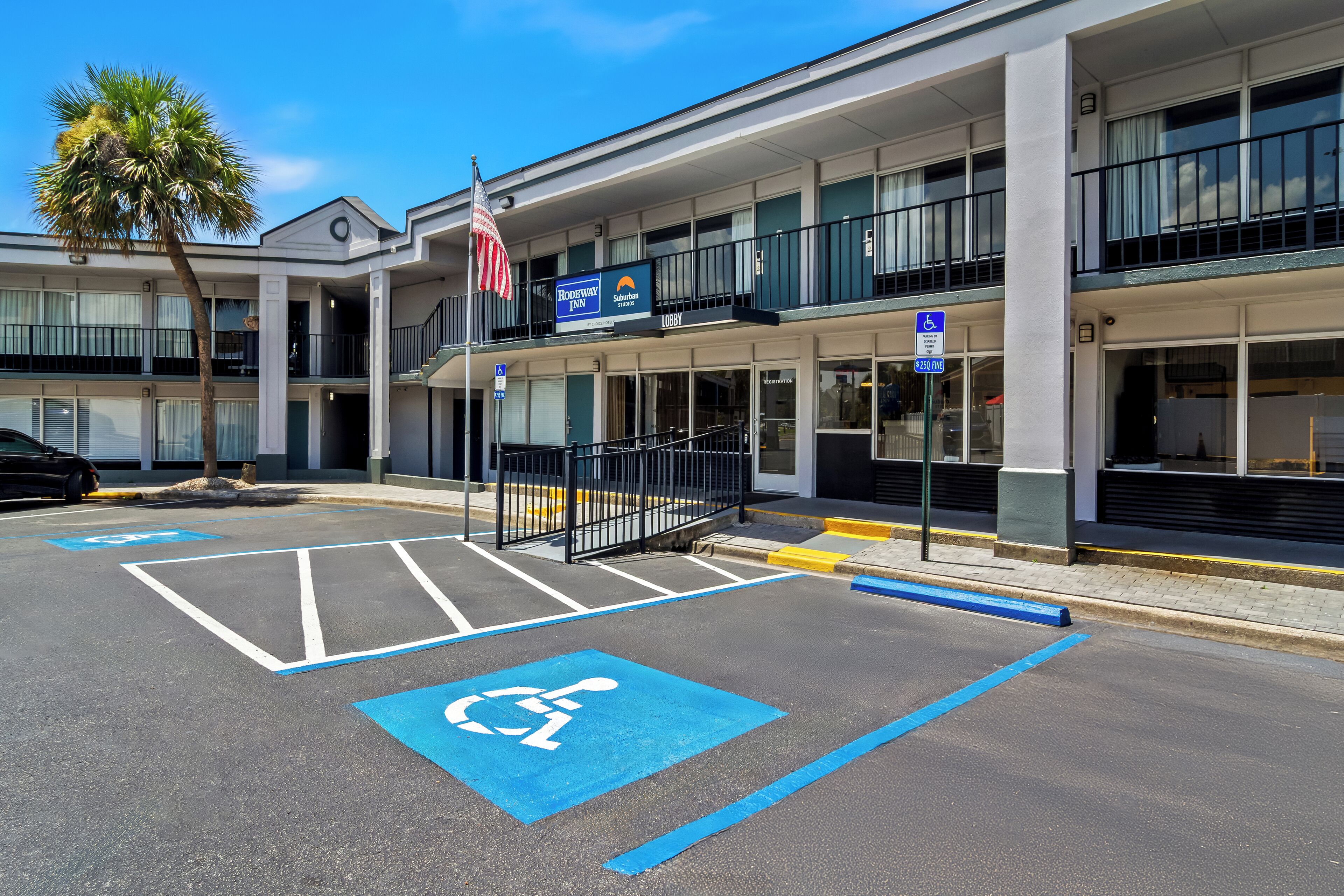 Un hotel con un edificio de dos pisos, una bandera y espacios de estacionamiento para discapacitados.
