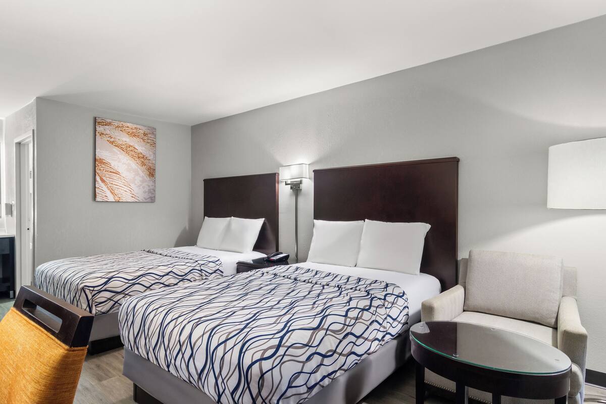 A hotel room with two beds, a sofa, a glass coffee table, and a wall-mounted lamp.